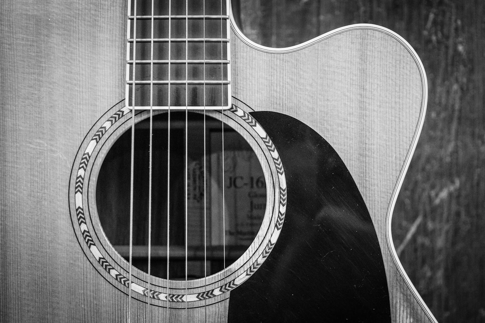 Detailed black and white photo of an acoustic guitar showcasing strings and sound hole.