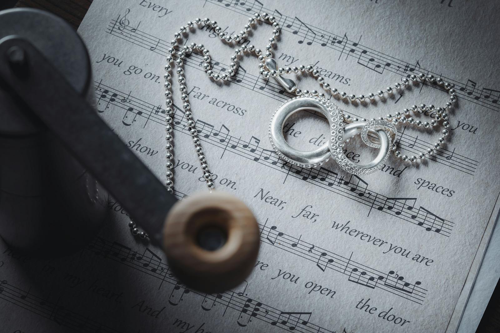 Closeup of a silver pendant resting on sheet music, symbolizing music and elegance.