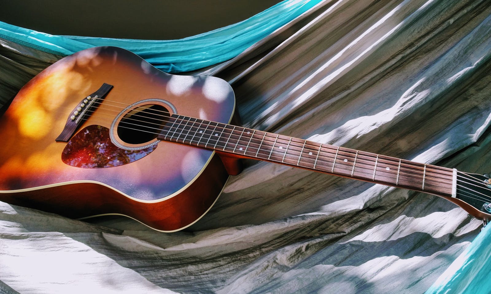 Beautiful acoustic guitar laying on a hammock under dappled sunlight, creating a serene atmosphere.