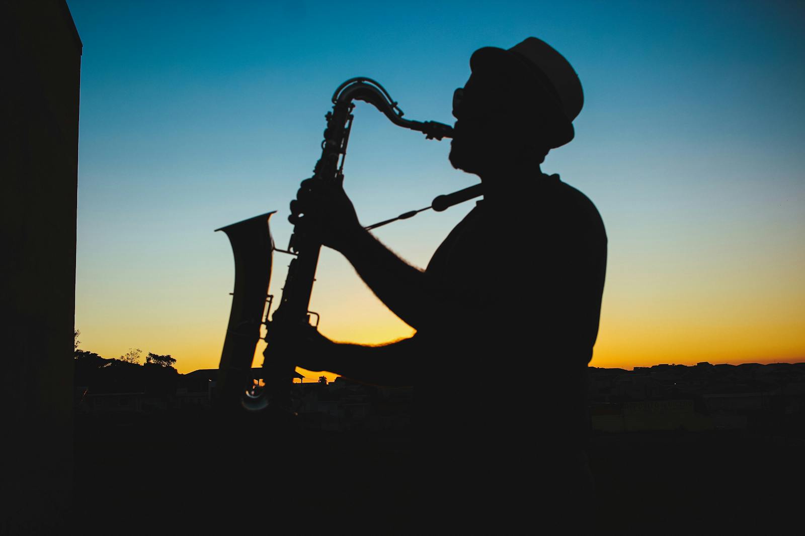 A man playing the saxophone silhouetted against a vibrant sunset sky.